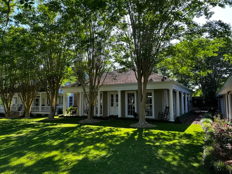 The white farmhouse and porch shaded by mature trees.
