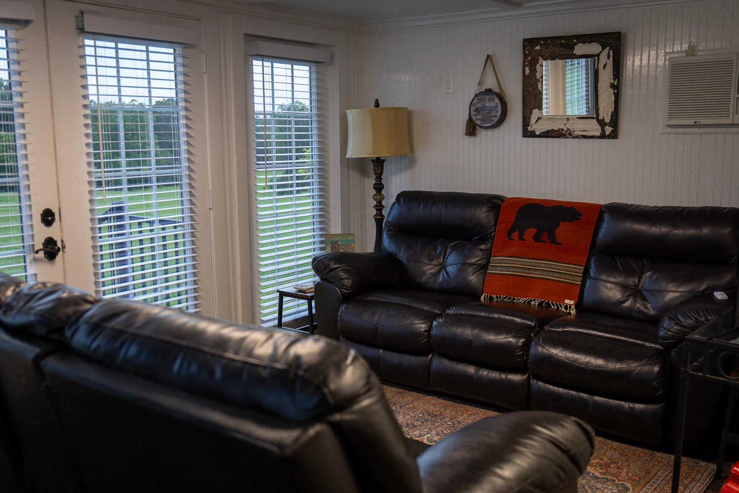 Black leather sofas in the Groom’s Quarters beside windows overlooking the lawn.