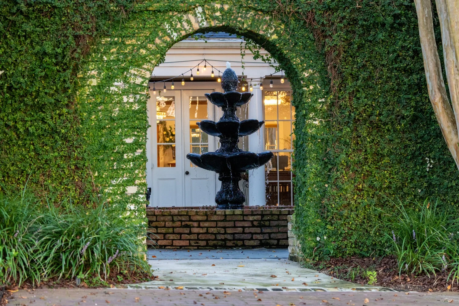 An ivy-covered brick arch framing a courtyard fountain and the open Oak Room doors.