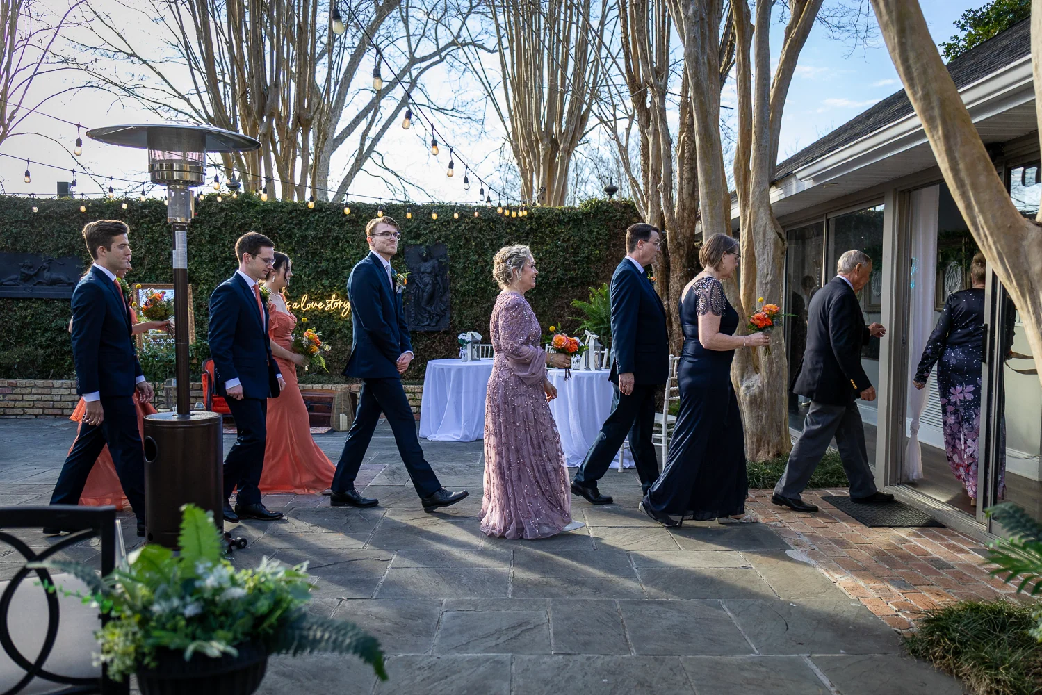 Wedding party members walking through Ivy Courtyard beneath string lights and toward the open doors.