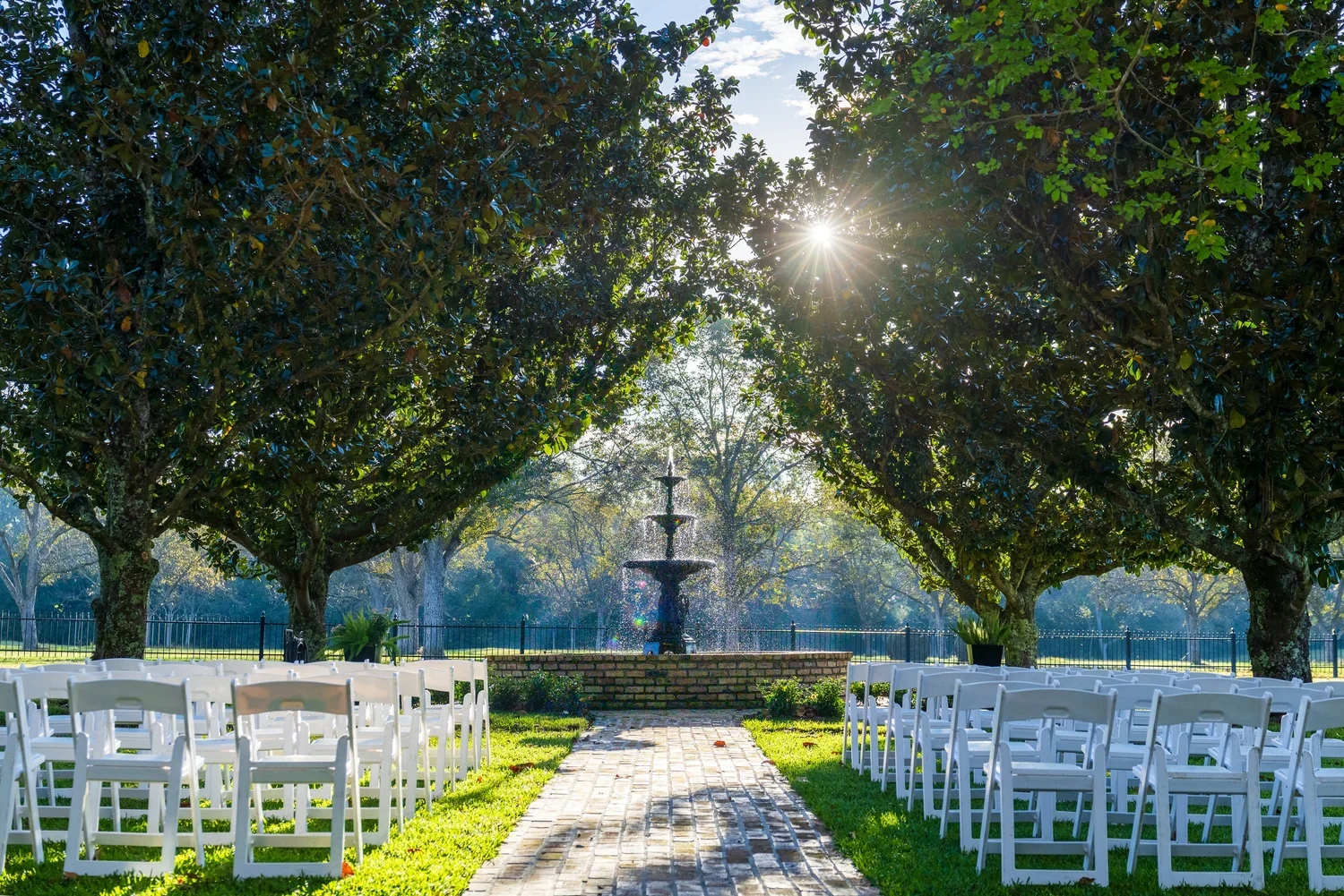 Sunlight through the trees over the brick aisle and ceremony chairs at Magnolia Fountain.