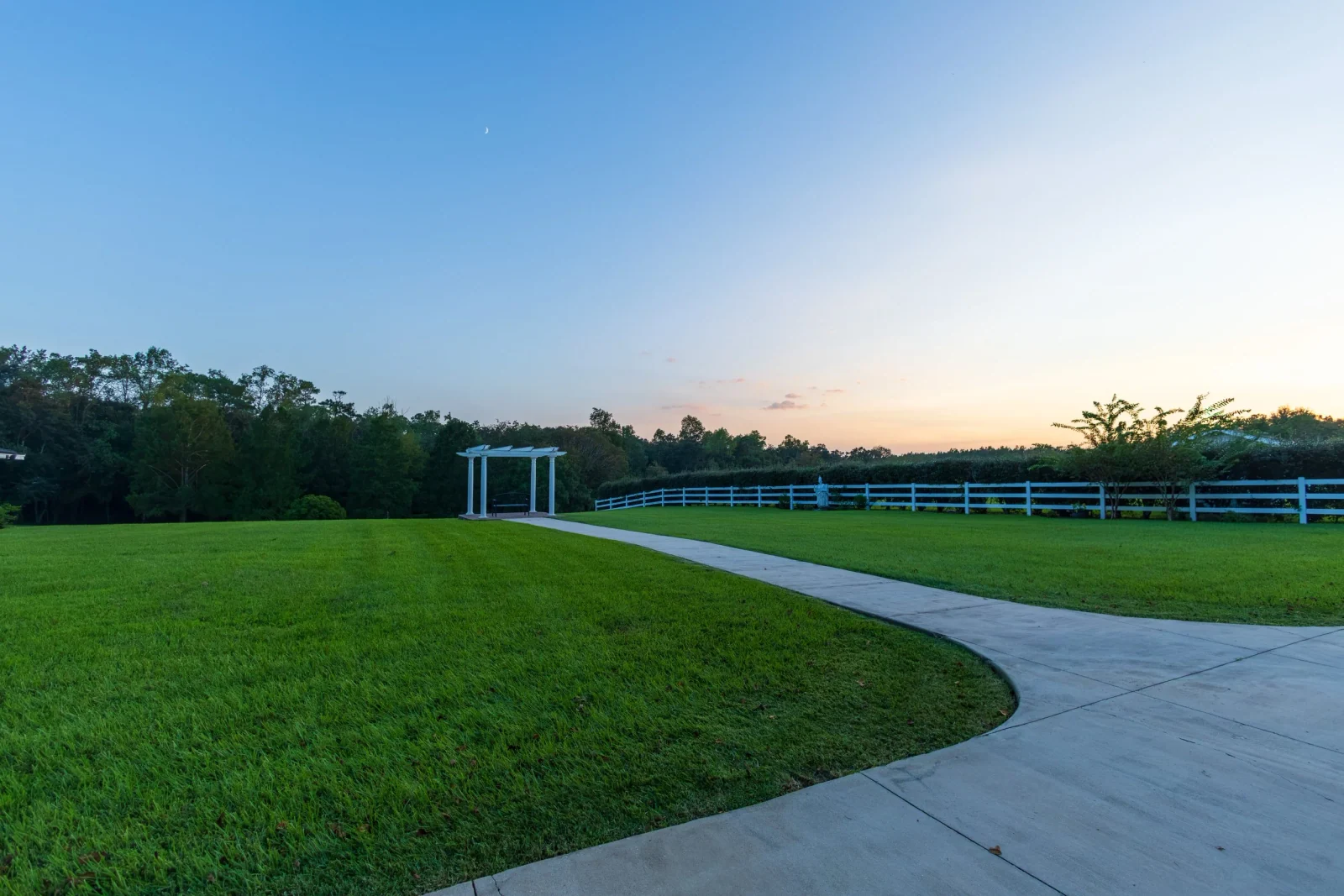 A broad lawn and a curved path lead toward the Waterfront Pergola at dusk.