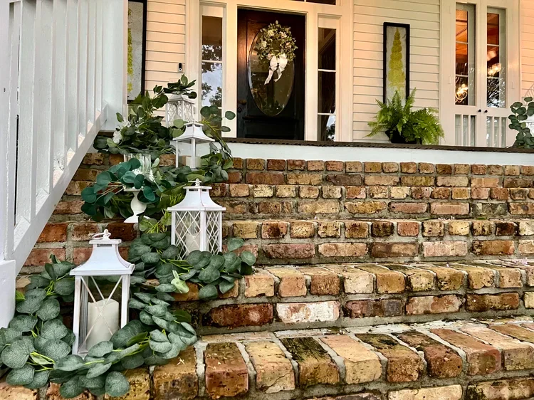 Brick porch steps decorated with greenery and lanterns.